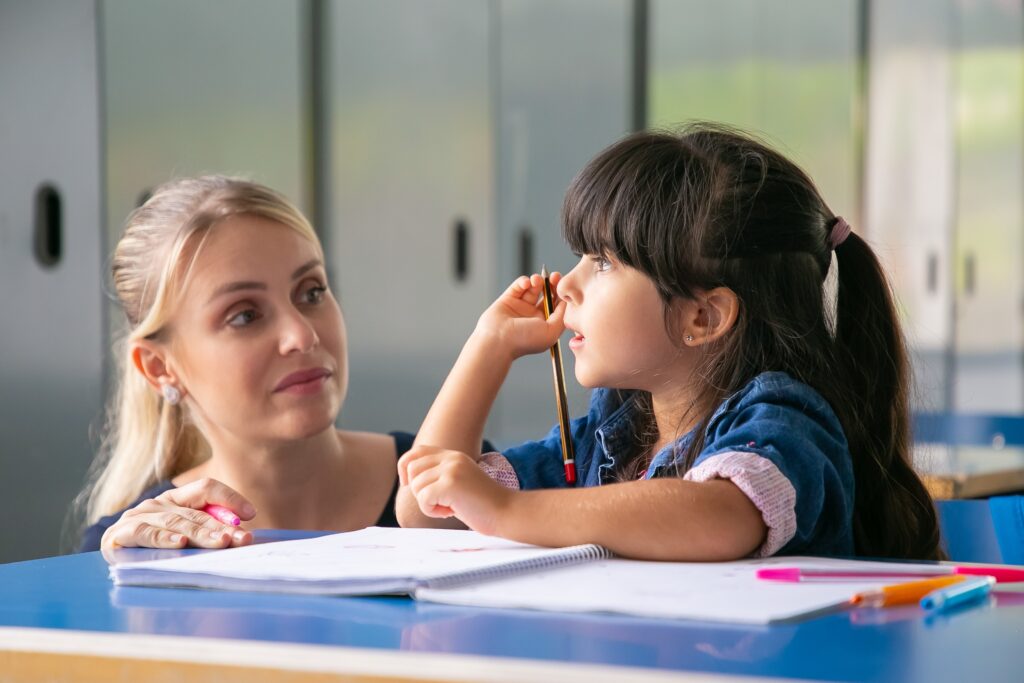 Serious female teacher discussing task with little pupil